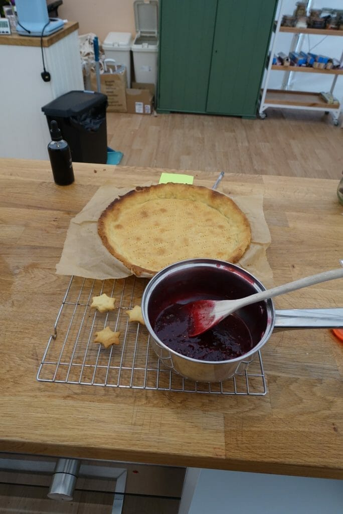 A saucepan of berry jam cooling next to the pastry