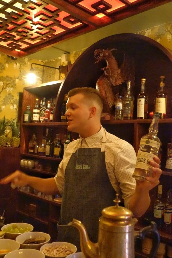 Nick behind the bar holding a bottle of Ford's gin