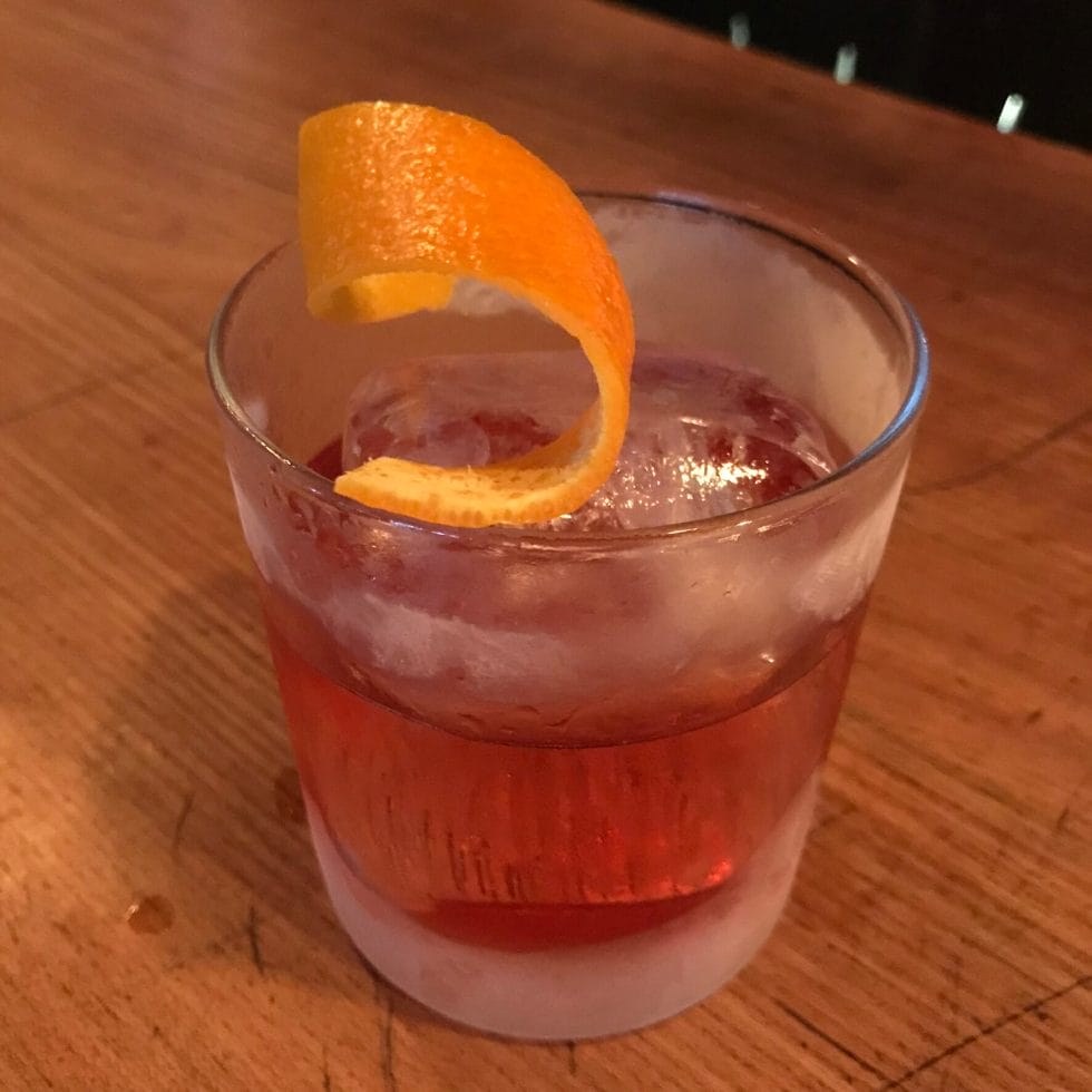 Negroni in a frozen glass with huge ice ball and orange peel