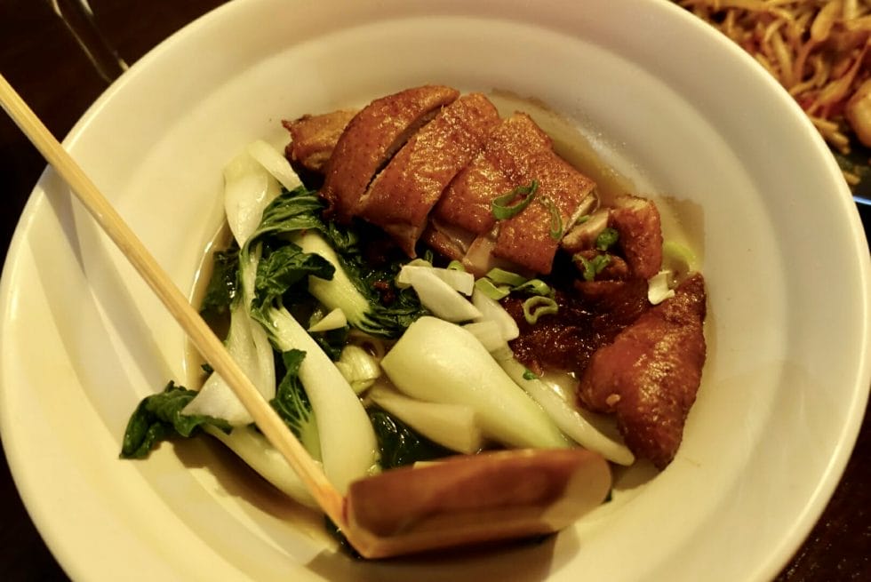 Roast duck ramen noodle soup with pak choi greens and wooden spoon
