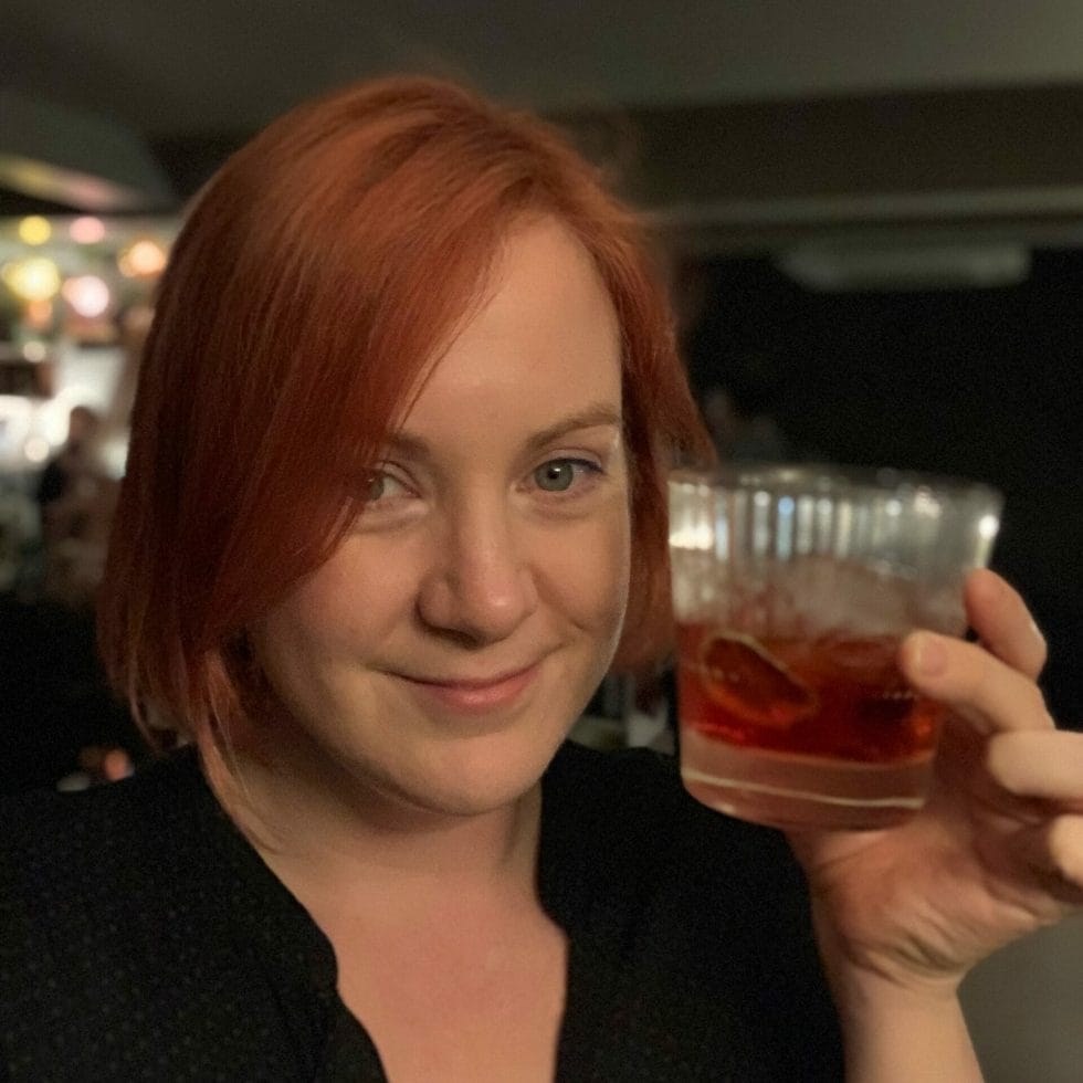Katie with red hair matching the negroni in her hand