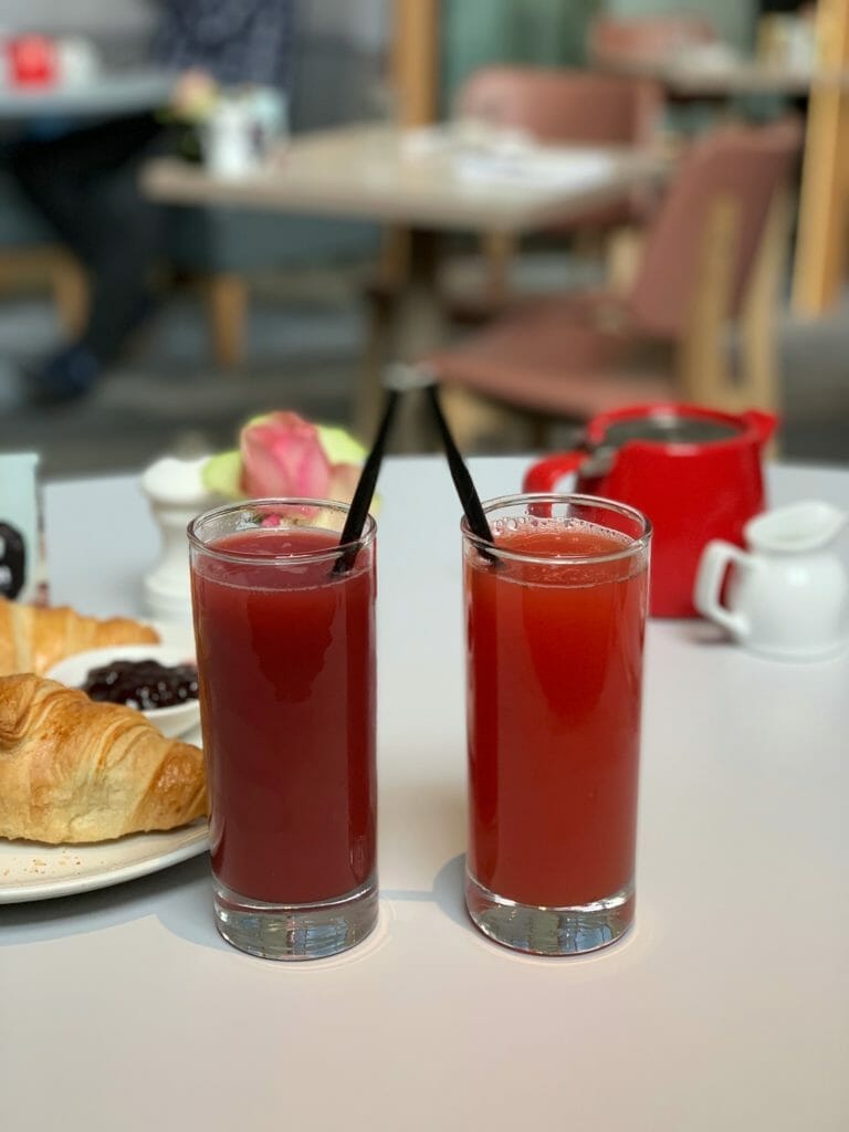Two red juices with the red tea pot in the background