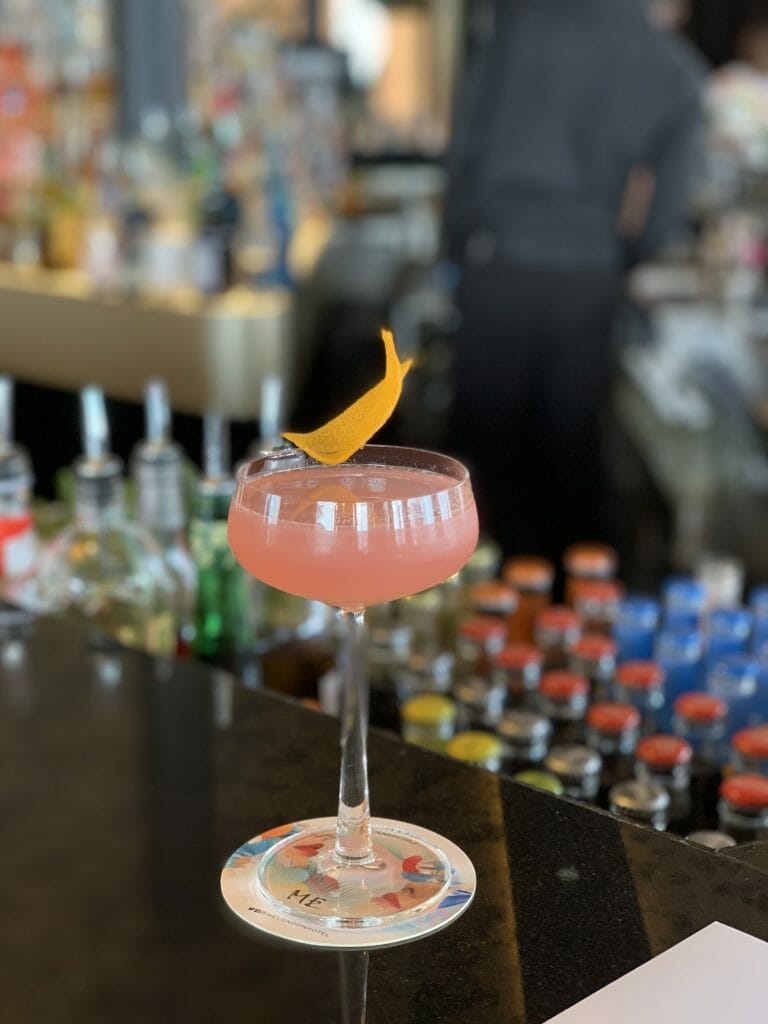 Coupe glass with pink cocktail garnished with orange peel