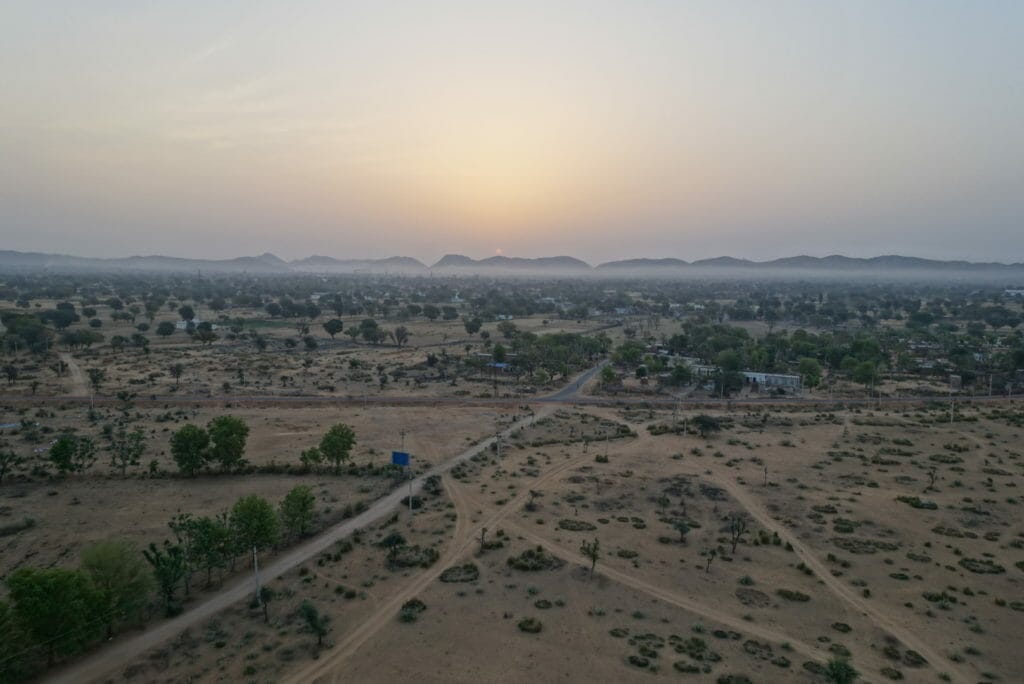 The sun rising over the distant Aravalli hills with countryside below