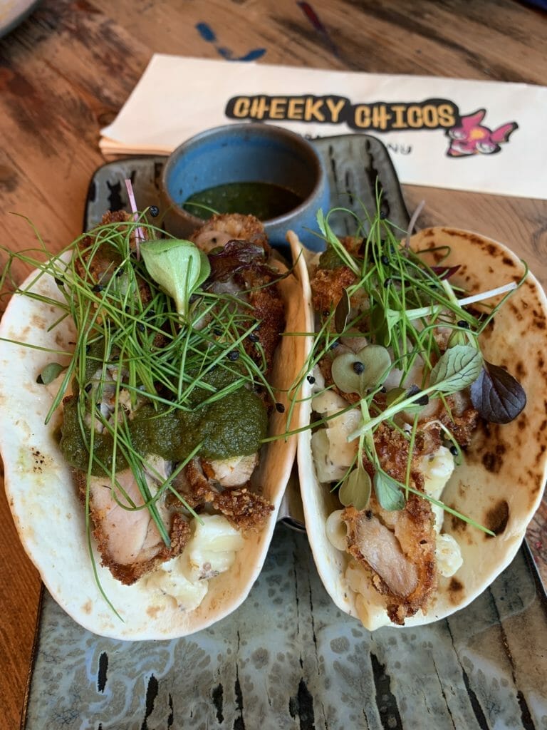 Two fried chicken tacos with extra green sauce on the side in a pot