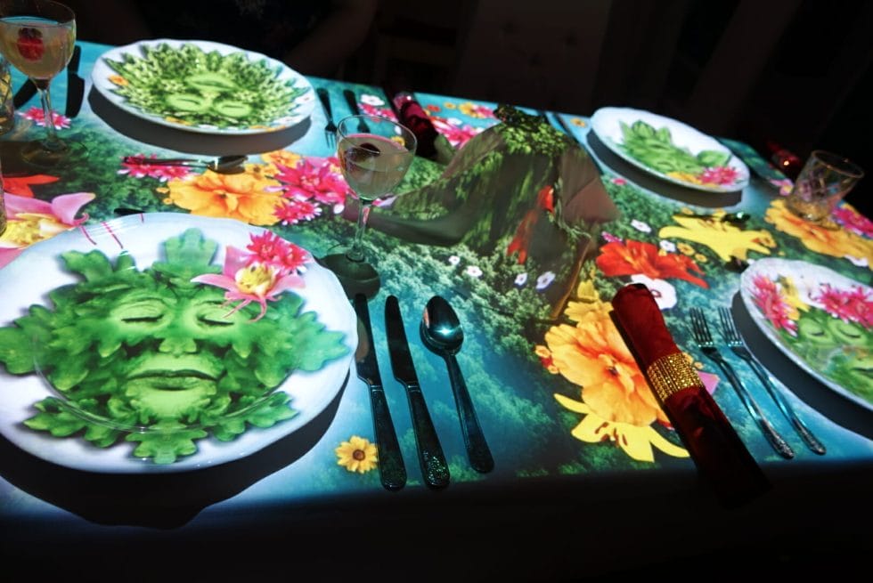 Table with images of faces and flowers projected on to it 