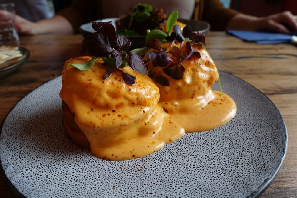 Two eggs Benedict stacks covered with chipotle hollandaise with micro herbs on top
