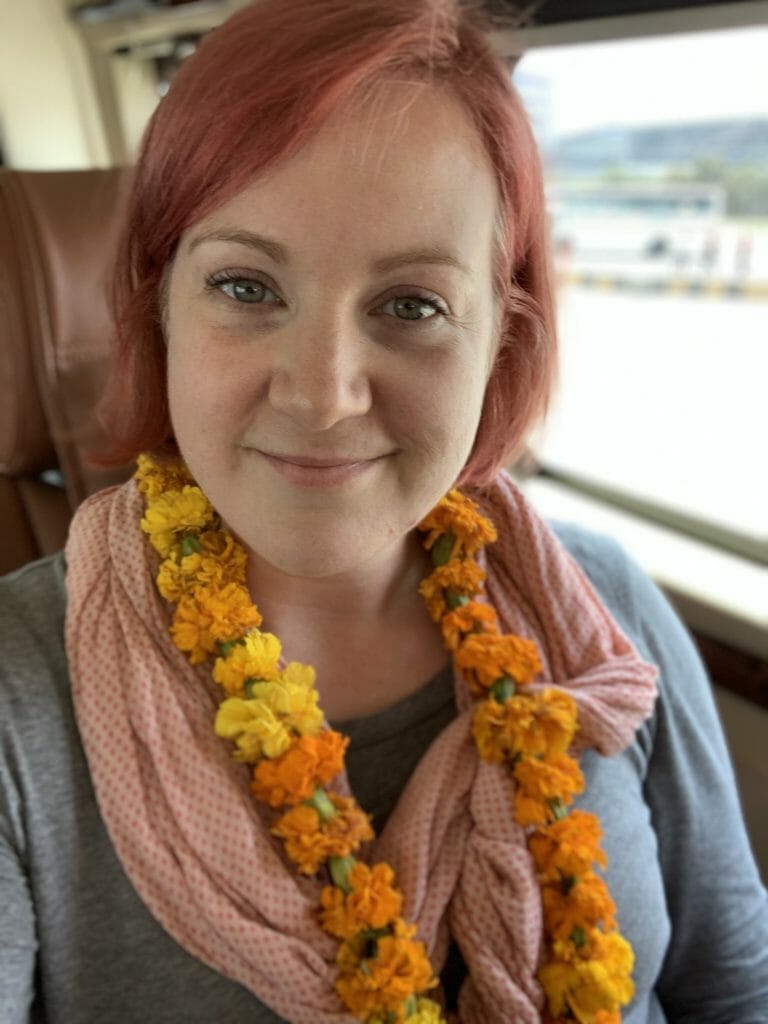 Katie wearing long sleeved grey top, pink scarf and flower garland in Delhi