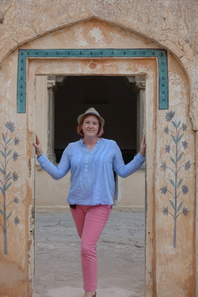 Katie in pink trousers, blue cotton top and hat in another doorway 