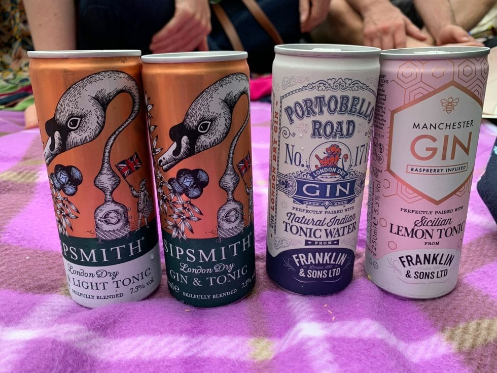 A collection of gins in a tin on a picnic blanket