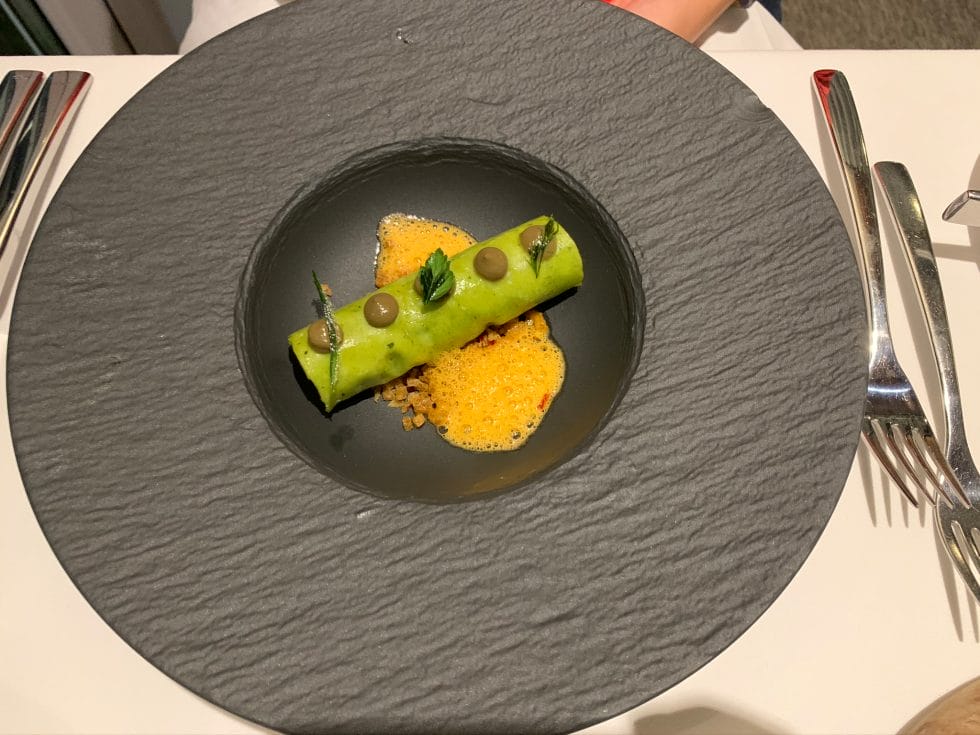 Black dish with green cannelloni and orange bisque in the middle