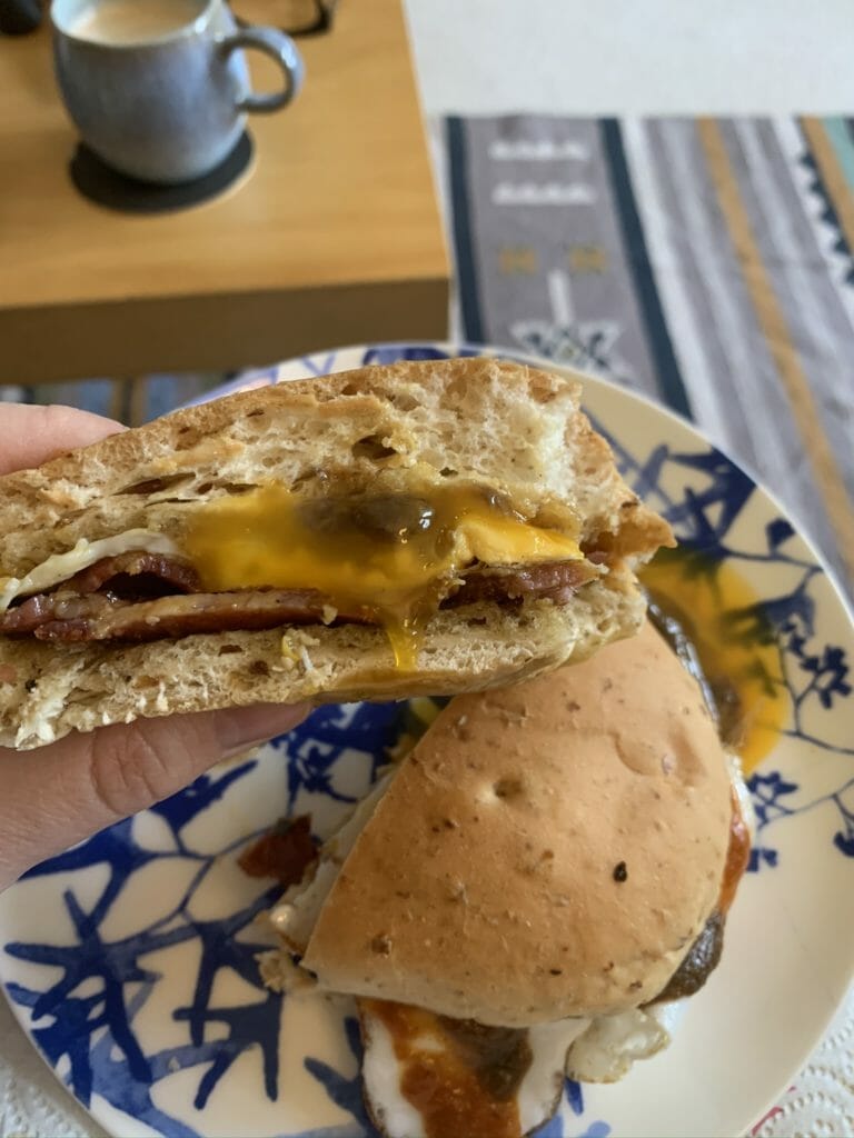 Side shot of the bacon sandwich cut in half with runny egg yolk