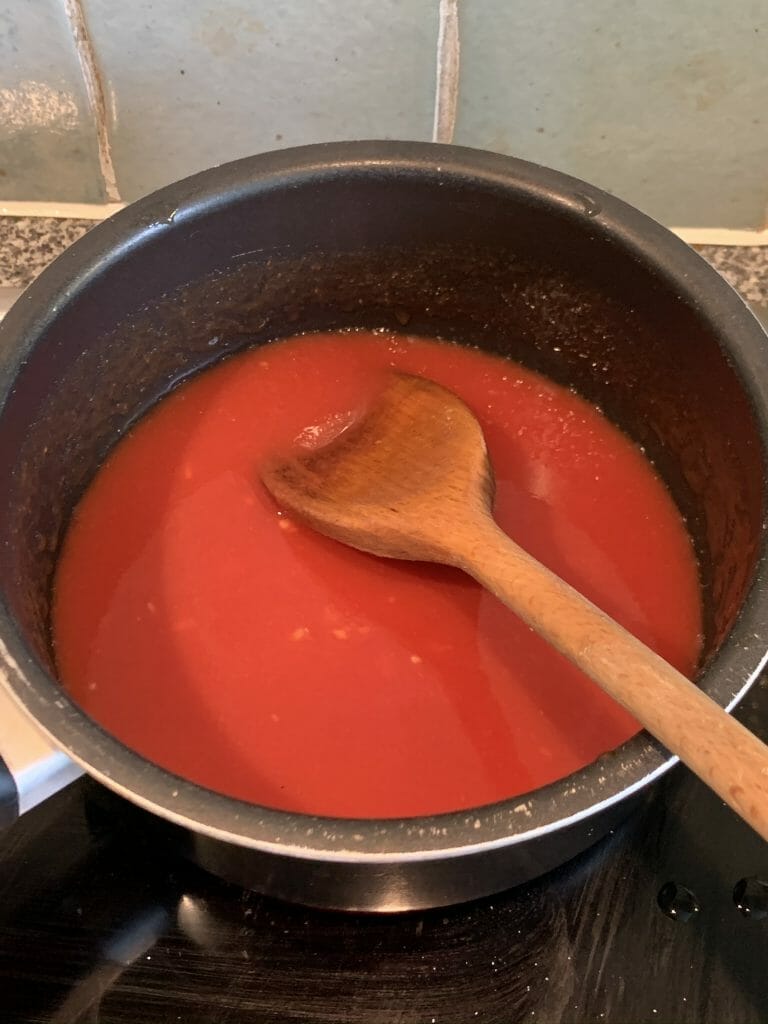 Tomato passata in a small pan with a wooden spoon