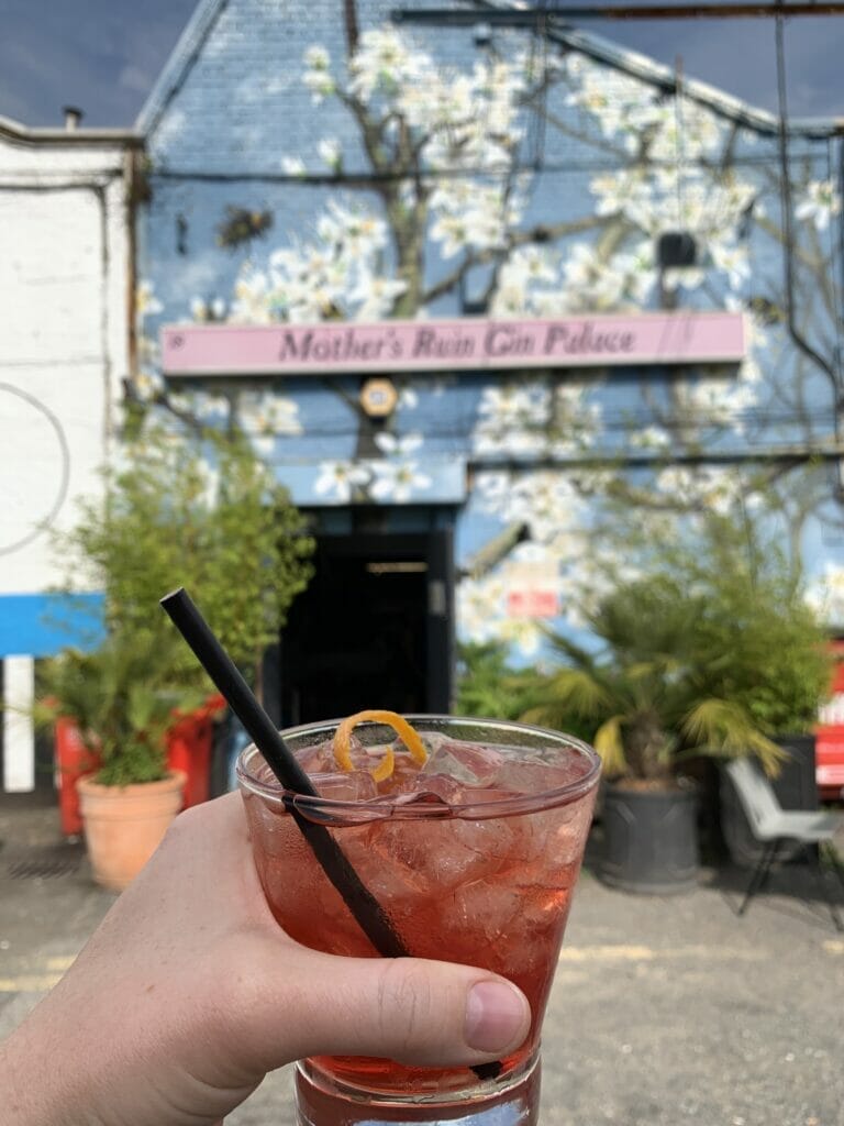 Mother's Ruin negroni in front of the distillery frontage painted with white blossom