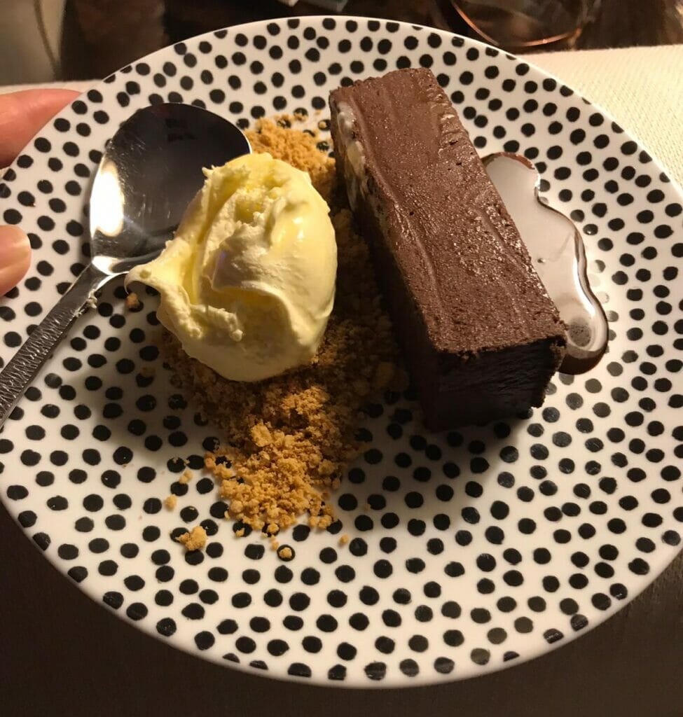 Chocolate Pave with clotted cream, chocolate sauce and cystallised peanutes on spotty plate