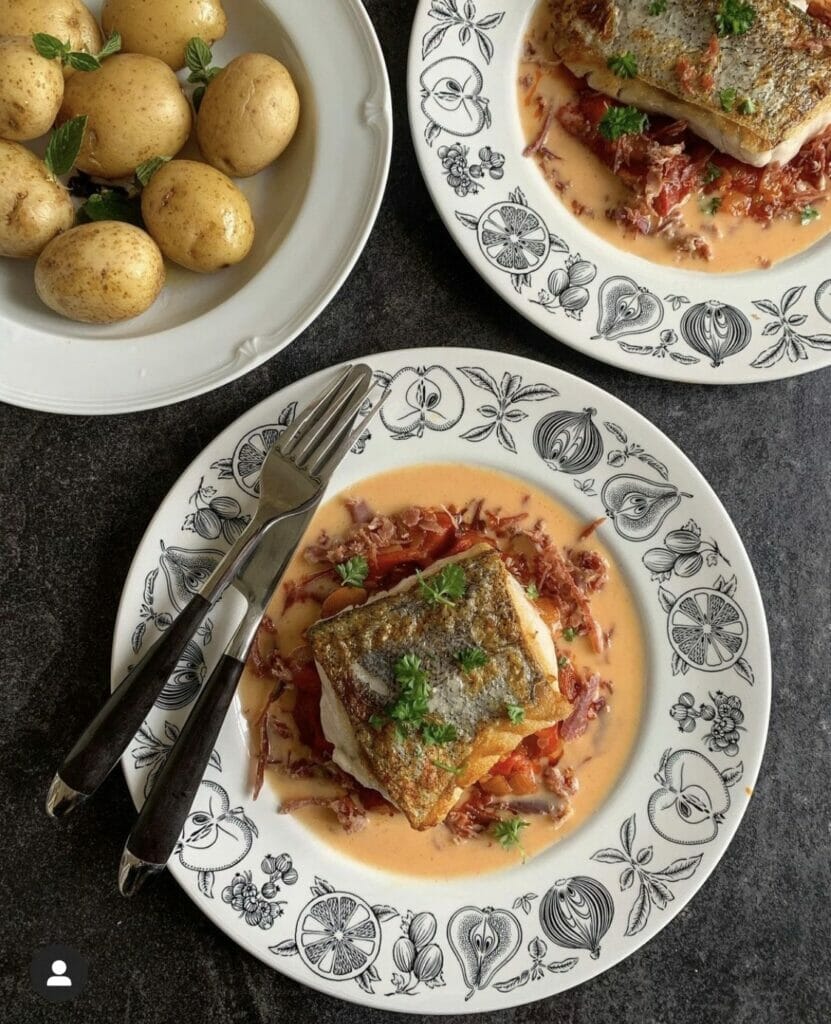 Hake on 2 plates with sauce and garnish and a bowl of new potatoes