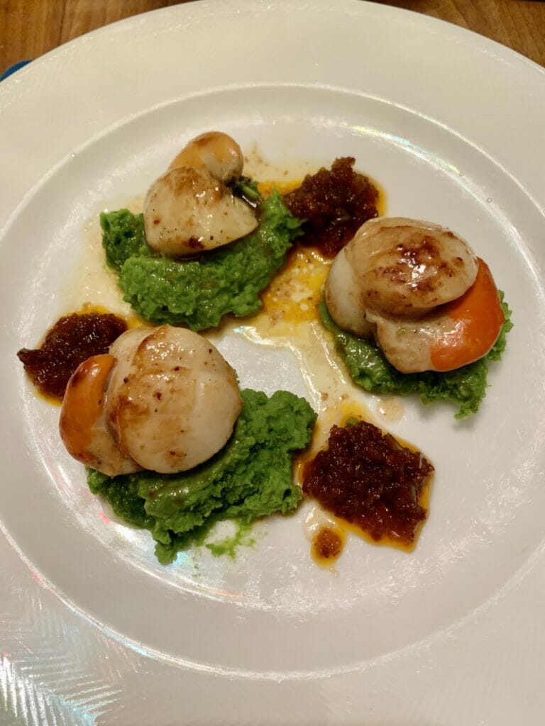 Three scallops plated on top of green pea puree with blobs of red chorizo jam